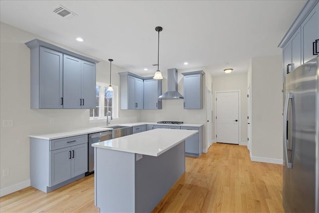 kitchen featuring wall chimney range hood, light hardwood / wood-style flooring, pendant lighting, a kitchen island, and appliances with stainless steel finishes