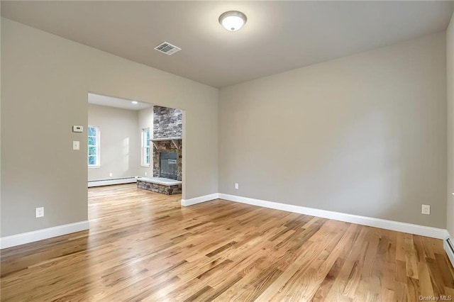 unfurnished living room with a stone fireplace, baseboard heating, and light hardwood / wood-style flooring