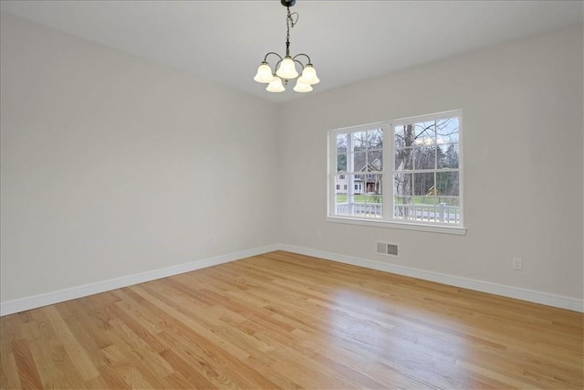 empty room with light wood-type flooring and a notable chandelier