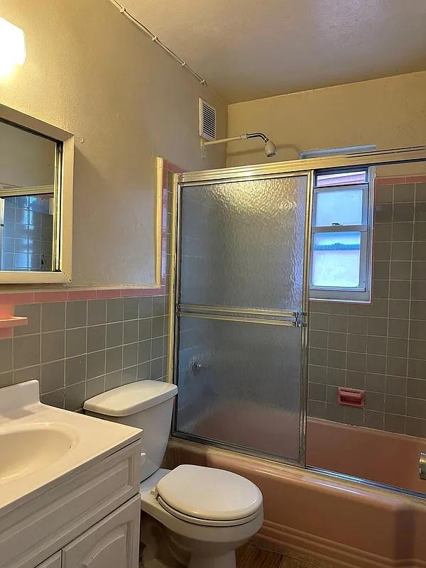 full bathroom with tile walls, vanity, enclosed tub / shower combo, and toilet