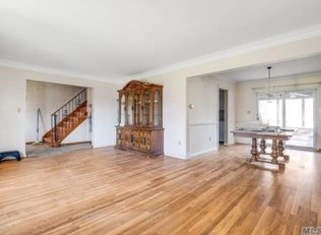 unfurnished living room featuring a chandelier, light hardwood / wood-style floors, and crown molding