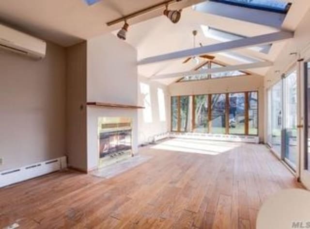 unfurnished living room featuring rail lighting, a baseboard radiator, lofted ceiling with beams, a wall mounted AC, and wood-type flooring