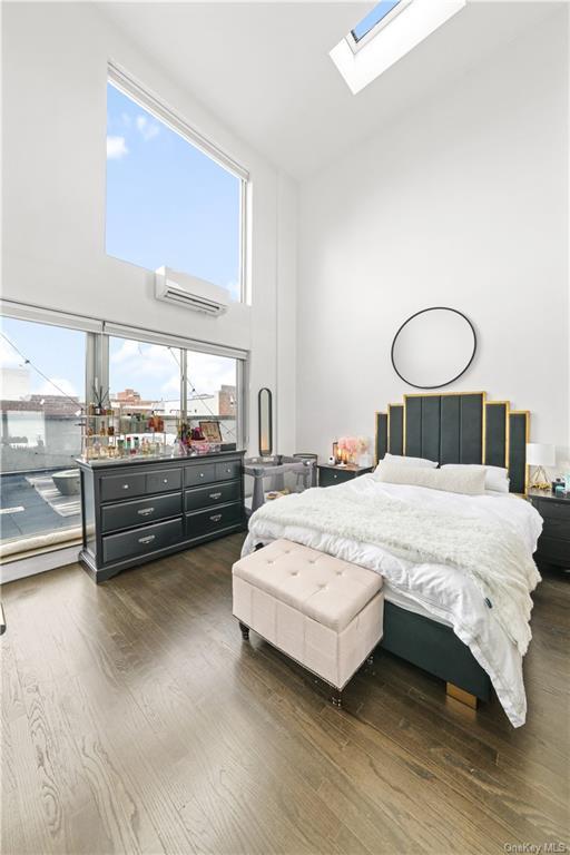 bedroom featuring high vaulted ceiling, a skylight, a wall unit AC, and dark wood-type flooring