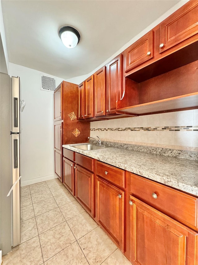 kitchen featuring backsplash, light tile patterned floors, sink, and stainless steel refrigerator