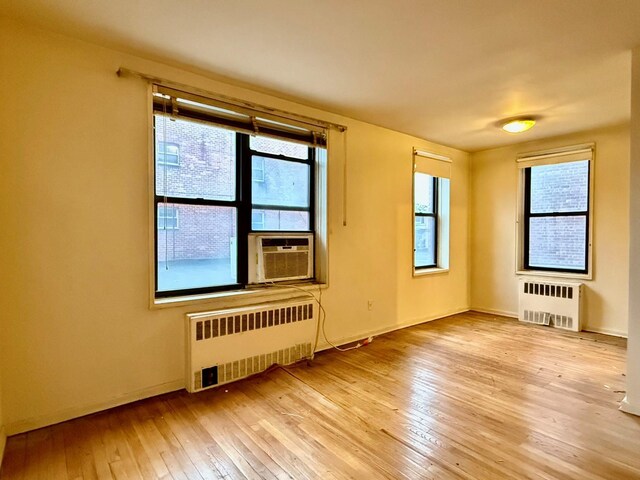 spare room with radiator heating unit, cooling unit, and light wood-type flooring