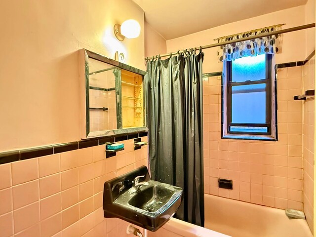 bathroom featuring shower / bathtub combination with curtain, sink, and tile walls