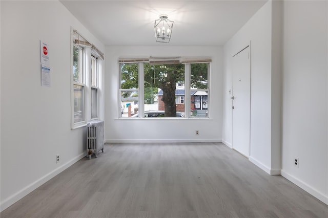 empty room featuring radiator, light hardwood / wood-style floors, and an inviting chandelier