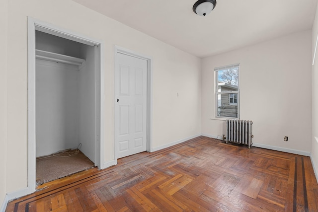 unfurnished bedroom featuring dark parquet floors, radiator, and a closet