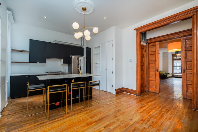 kitchen with a breakfast bar, stainless steel fridge, a center island with sink, and decorative light fixtures