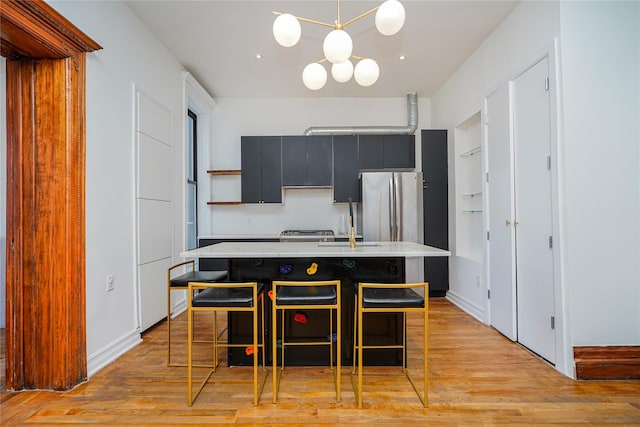 kitchen featuring a kitchen breakfast bar, light wood-type flooring, pendant lighting, a center island with sink, and stainless steel refrigerator