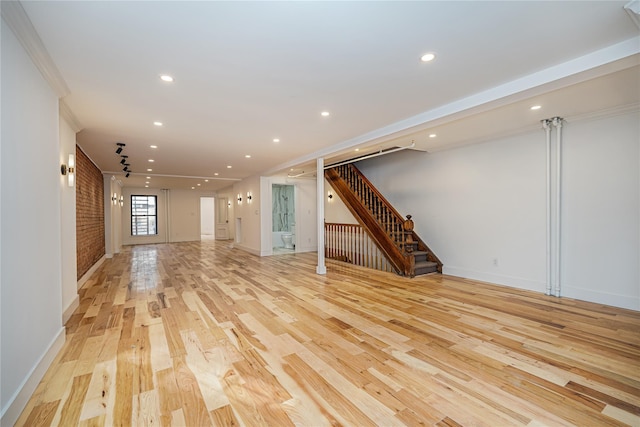 unfurnished living room with ornamental molding, brick wall, and light wood-type flooring