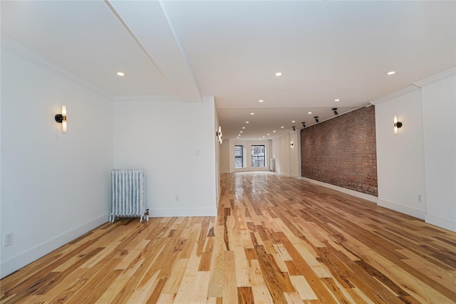 interior space with light hardwood / wood-style flooring, radiator, crown molding, and brick wall