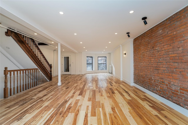 unfurnished living room with brick wall and light hardwood / wood-style flooring