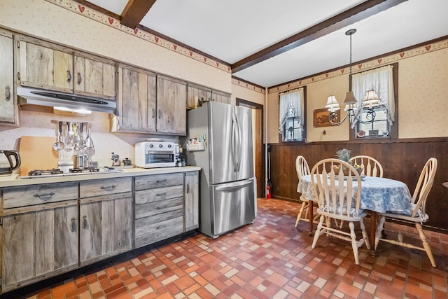 kitchen featuring beamed ceiling, stainless steel appliances, hanging light fixtures, and wood walls