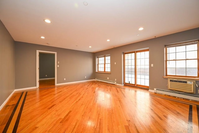 spare room featuring light wood-type flooring, an AC wall unit, and baseboard heating