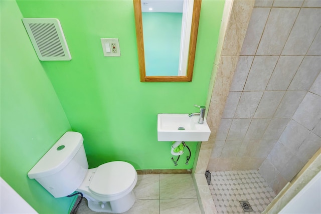 bathroom with toilet, sink, tile patterned flooring, and tiled shower