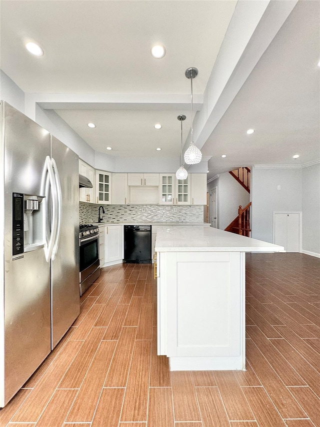 kitchen with pendant lighting, appliances with stainless steel finishes, white cabinetry, wall chimney range hood, and backsplash