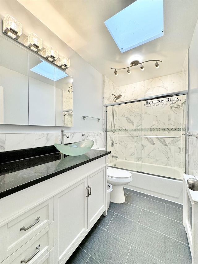 full bathroom featuring toilet, tiled shower / bath, tile walls, vanity, and a skylight