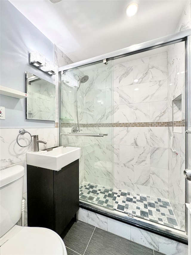 bathroom featuring toilet, a shower with shower door, tile walls, tile patterned floors, and vanity