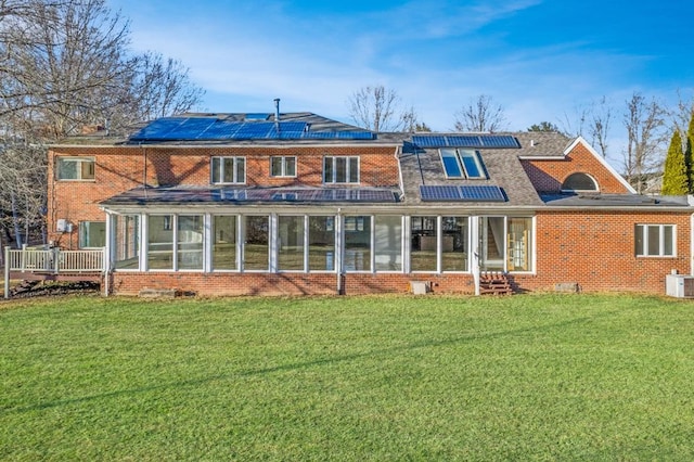 back of property featuring a sunroom, a yard, and solar panels