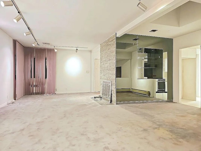 empty room with a stone fireplace, concrete flooring, and track lighting