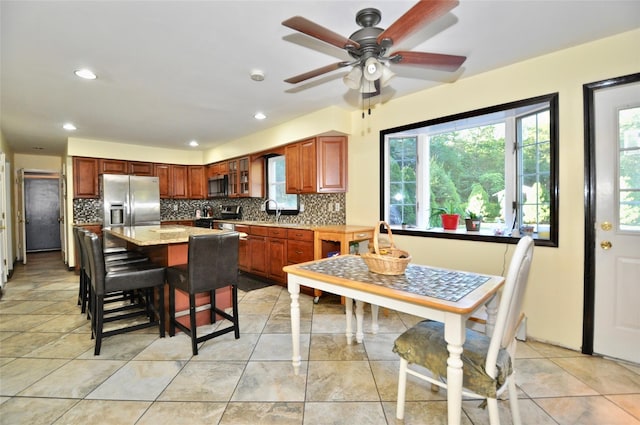 kitchen featuring a breakfast bar area, decorative backsplash, light stone countertops, a kitchen island, and stainless steel appliances