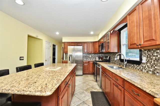 kitchen with a breakfast bar, a center island, sink, light stone countertops, and appliances with stainless steel finishes