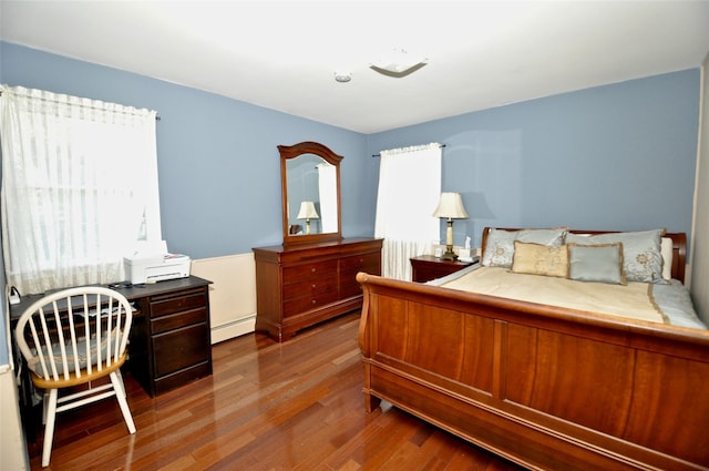 bedroom featuring hardwood / wood-style flooring, multiple windows, and a baseboard heating unit