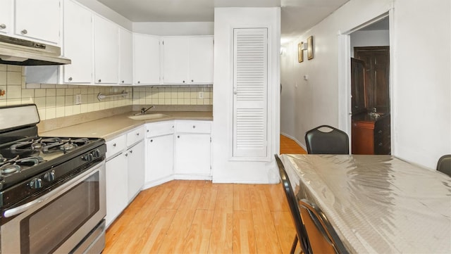 kitchen featuring light wood-type flooring, backsplash, stainless steel gas range, sink, and white cabinetry