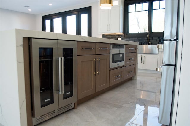 kitchen featuring stainless steel refrigerator, white cabinetry, sink, and wine cooler