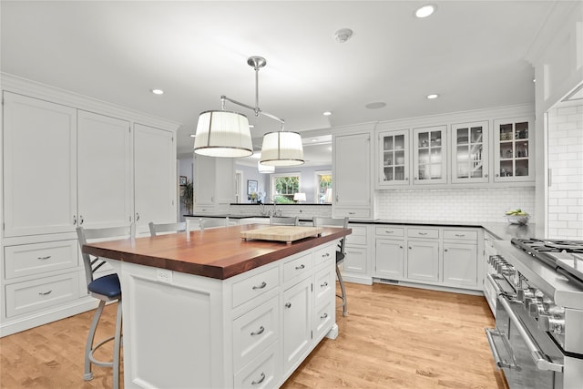 kitchen featuring white cabinetry, butcher block countertops, backsplash, a breakfast bar, and high end range