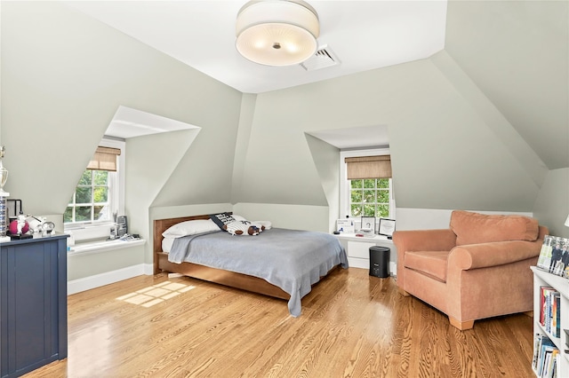 bedroom with vaulted ceiling, light wood-type flooring, and multiple windows