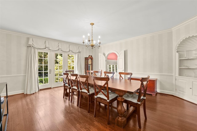 dining room featuring dark wood-type flooring, french doors, an inviting chandelier, built in shelves, and ornamental molding