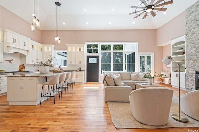 living room with ceiling fan, sink, high vaulted ceiling, and light wood-type flooring