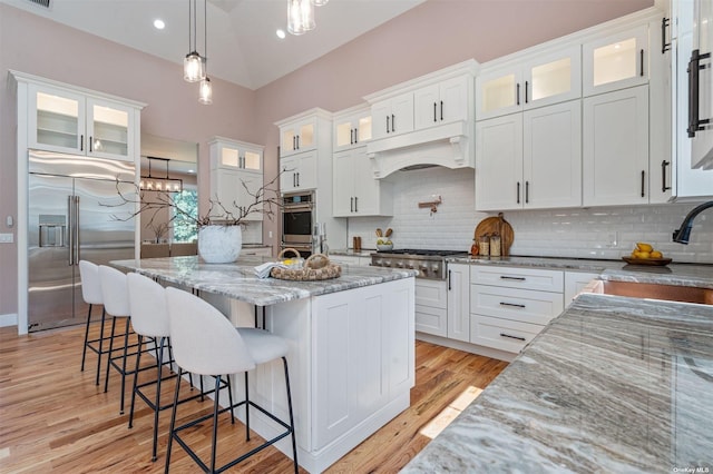 kitchen with stainless steel appliances, white cabinets, a kitchen island, hanging light fixtures, and lofted ceiling