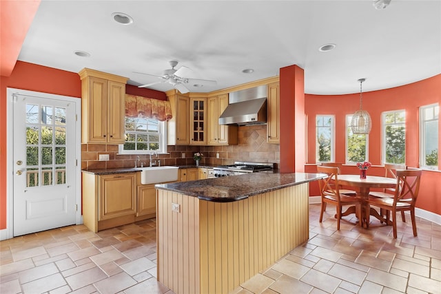 kitchen with pendant lighting, plenty of natural light, wall chimney range hood, and sink