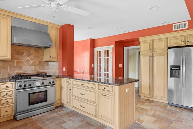 kitchen featuring stainless steel appliances, wall chimney range hood, backsplash, kitchen peninsula, and dark stone countertops