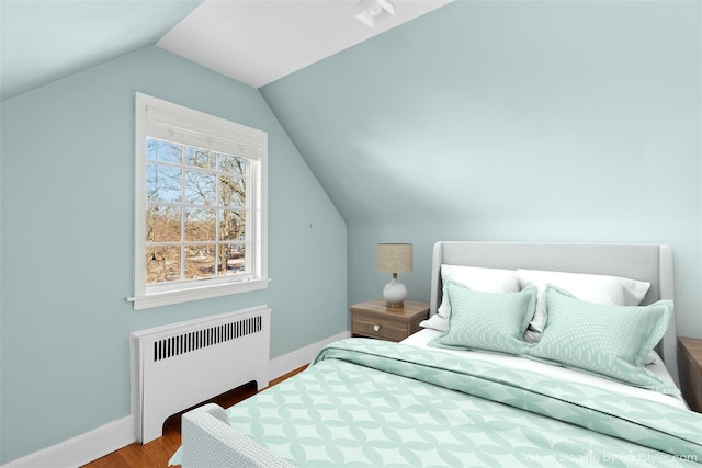 bedroom with radiator heating unit, light hardwood / wood-style floors, and vaulted ceiling