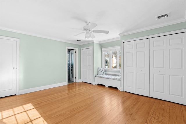 unfurnished bedroom with hardwood / wood-style flooring, ceiling fan, crown molding, and multiple closets