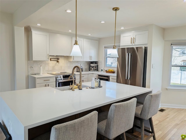 kitchen with backsplash, stainless steel appliances, a kitchen island with sink, decorative light fixtures, and white cabinetry