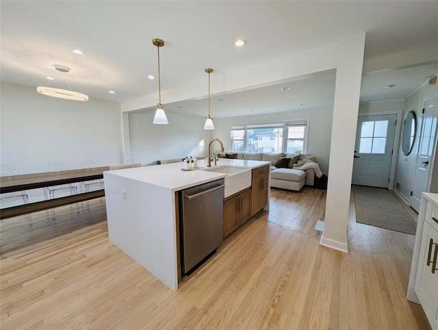 kitchen featuring sink, stainless steel dishwasher, pendant lighting, a center island with sink, and light wood-type flooring