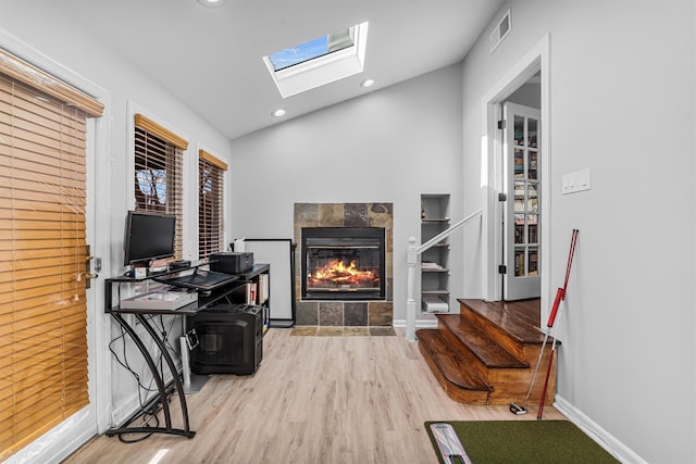 interior space with light hardwood / wood-style flooring, a tile fireplace, and vaulted ceiling with skylight