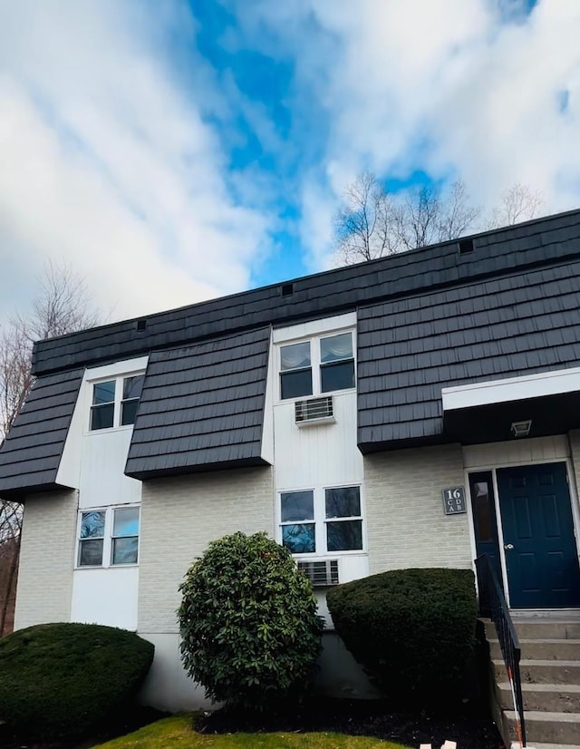 exterior space featuring entry steps, mansard roof, and brick siding