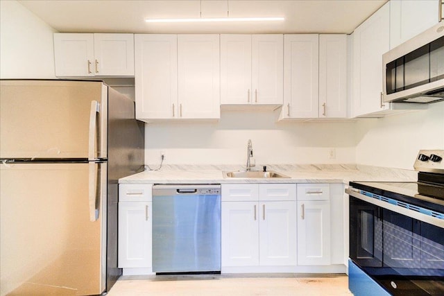 kitchen with white cabinets, appliances with stainless steel finishes, light stone counters, and sink