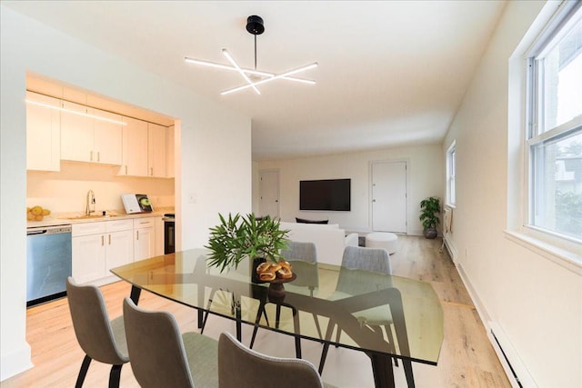 dining area with light wood finished floors, baseboard heating, a wealth of natural light, and an inviting chandelier