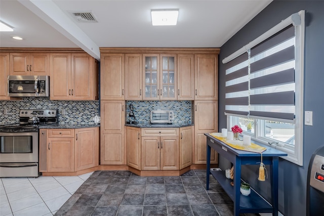 kitchen with decorative backsplash, dark stone counters, and appliances with stainless steel finishes