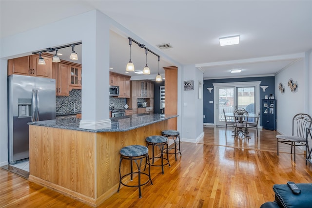 kitchen featuring tasteful backsplash, light hardwood / wood-style flooring, kitchen peninsula, dark stone counters, and appliances with stainless steel finishes