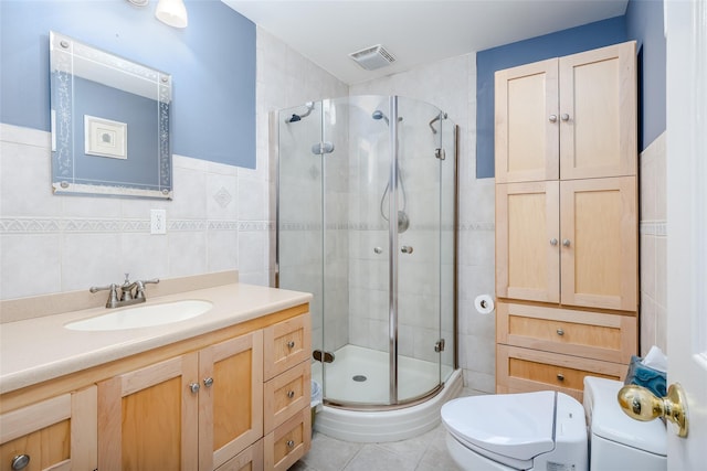 bathroom featuring tile patterned flooring, toilet, a shower with door, vanity, and tile walls