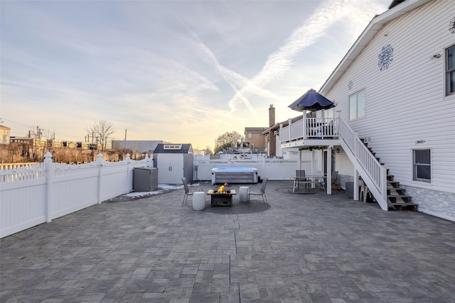 patio terrace at dusk featuring a storage unit, an outdoor fire pit, and a wooden deck