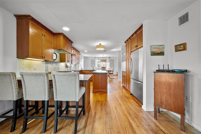 kitchen featuring a breakfast bar, light hardwood / wood-style flooring, stainless steel fridge, kitchen peninsula, and backsplash